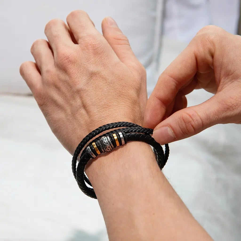 Person adjusting a black braided leather bracelet on their wrist with a white background